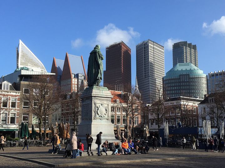 People resting by the statue of William of Orange on Plein, with old houses and modern towers behind.